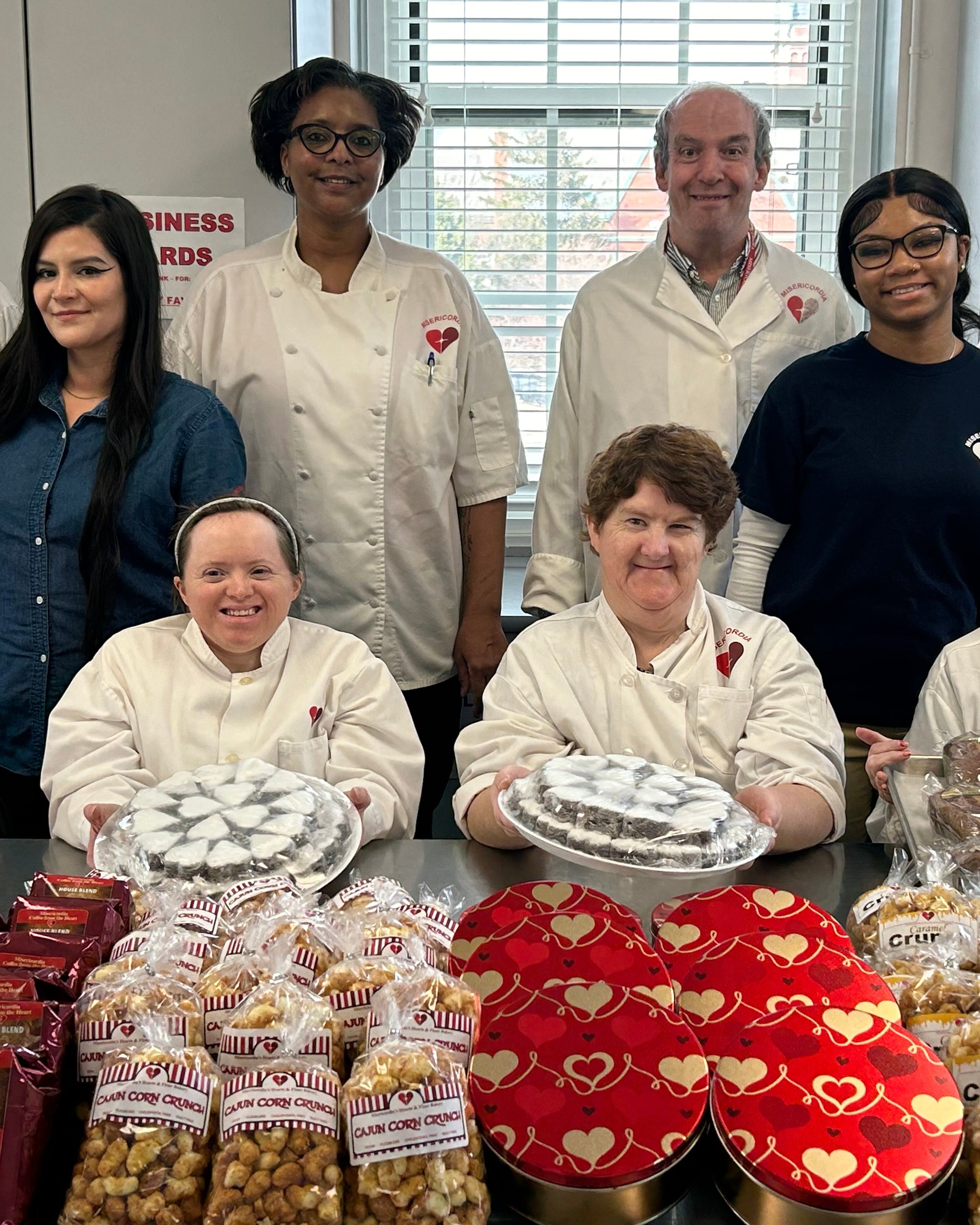 Group of people with baked goods and heart-shaped items in a kitchen setting